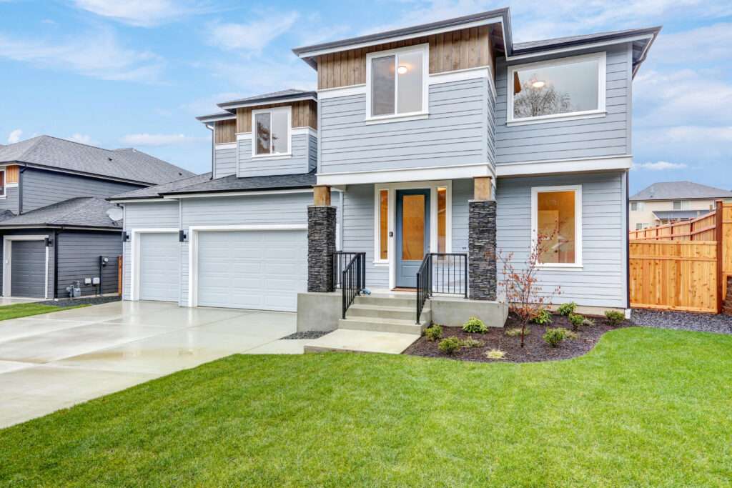 Modern two-story house with gray siding, large windows, and a double garage. The well-manicured lawn and clear blue sky create a welcoming, serene atmosphere.