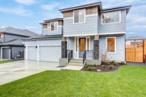 Modern two-story house with gray siding, large windows, and a double garage. The well-manicured lawn and clear blue sky create a welcoming, serene atmosphere.